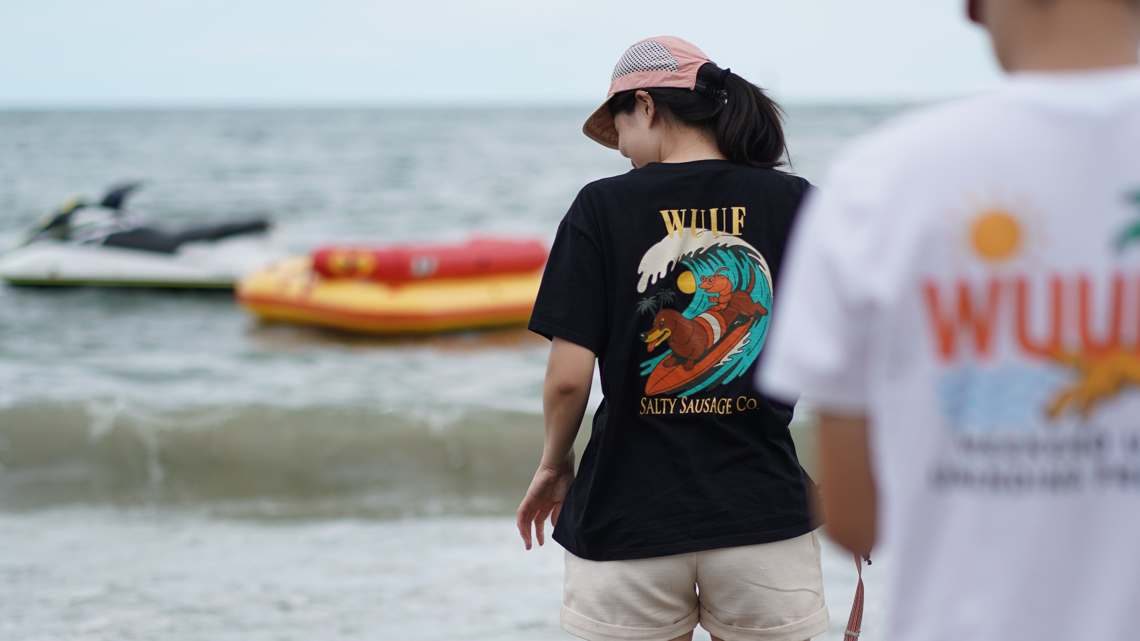 Two people lying on a beach with a large wave in the background